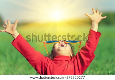 Happy little girl with hands in the air wearing big sunglasses and looking at the sun