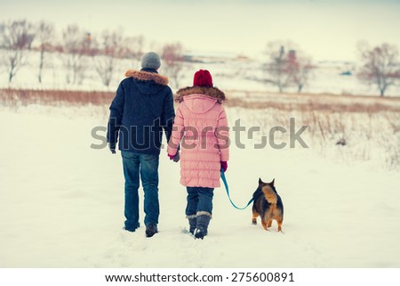 Young couple in love with dog walking in the snowy field back to camera