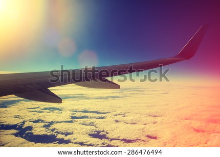 Airplane flying above clouds at pink sunrise