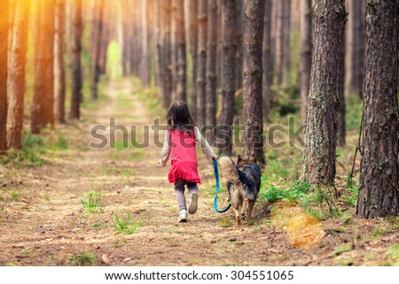 Little girl walking with big dog  in the pine forest