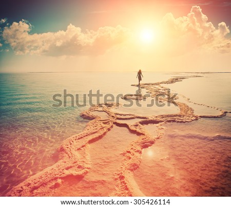 Silhouette of young woman walking on Dead Sea at sunrise