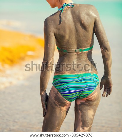 Woman smearing mud mask on the body back to camera