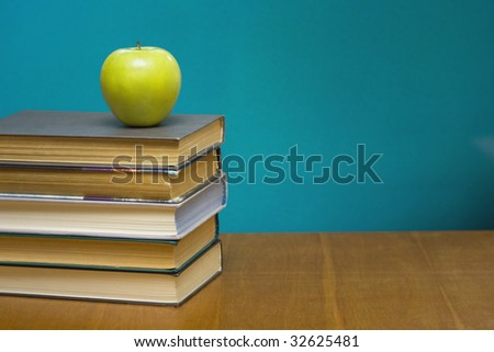A green apple and  books on the desk.