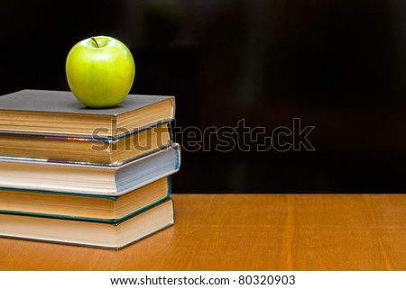 A green apple and  books on the desk. Blackboard as background.