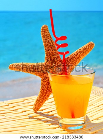 Starfish, glass of orange cocktail against the blue sea
