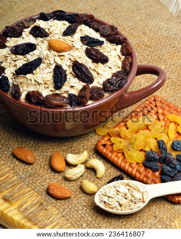 Oatmeal in ceramic plate, spoon, raisins, cashews and almonds on the sacking background