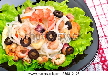 rice noodles with seafood, olives and green salad on black plate
