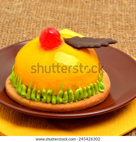 Christmas delicious yellow cake with cherry on ceramic saucer on yellow napkin on sacking background