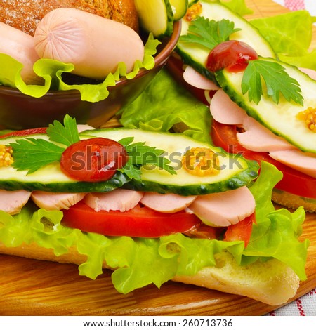 Big appetizing fast food baguette sandwich with lettuce, tomato and frankfurter on the board. Junk food