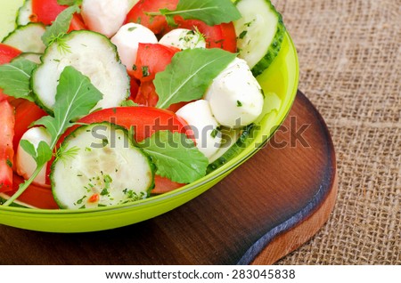 Fresh salad with mozzarella cheese, tomatoes, cucumber and rocket salad on the cutting board