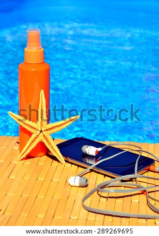 Cell phone, sun spray, head phones and starfish near blue water
