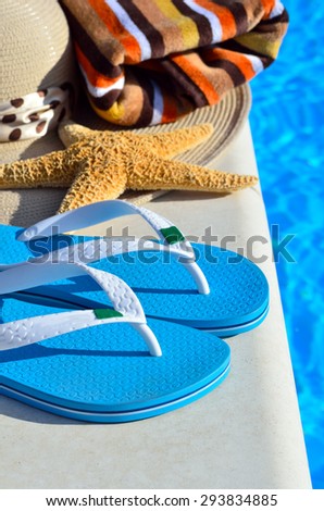 Woman beach hat, bright towel and blue flip-flops against blue swimming pool