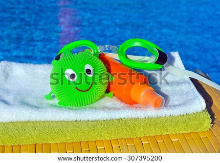 Bath towels, goggles and sun spray, toy against blue water in the swimming pool