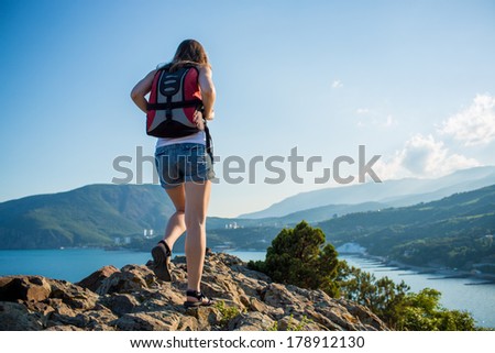 Young tourist woman is hiking on the top of the mounting and looking at a beautiful sea landscape