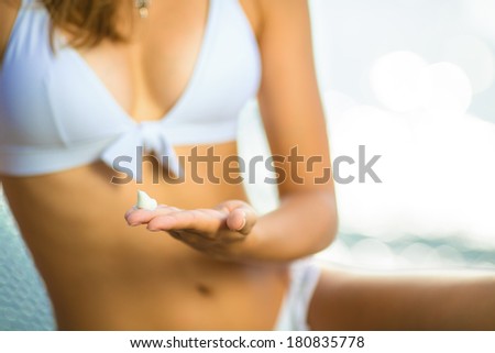 Young caucasian woman is holding some sunscreen on her hand before applying it to protect her skin near the sea on a summer day. Healthy lifestyle concept.