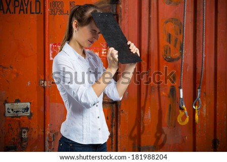 Young business woman on a containers background is hitting herself with a clipboard in despair and anxiety because of a logistics management problem