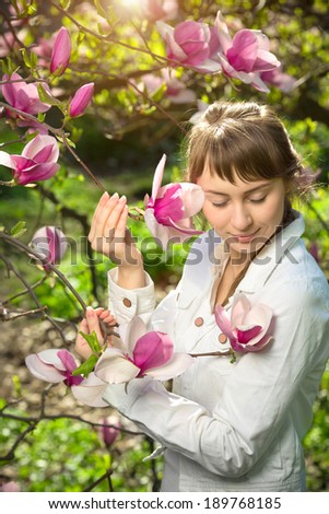 Beautiful happy young woman enjoying spring morning near the blooming magnolia tree. Natural beauty spring concept.