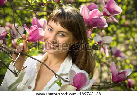 Beautiful happy young woman enjoying spring morning near the blooming magnolia tree. Natural beauty spring concept.