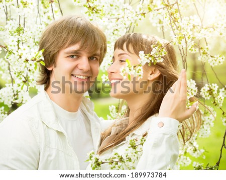 Happy young couple in love in a spring blossoming apple tree branches on a sunny day in the park.