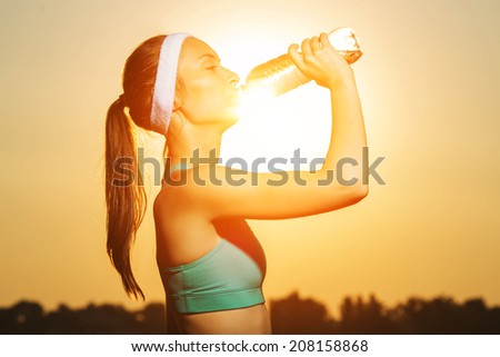 Beautiful athletic woman is drinking pure water from the bottle refreshing herself after running.