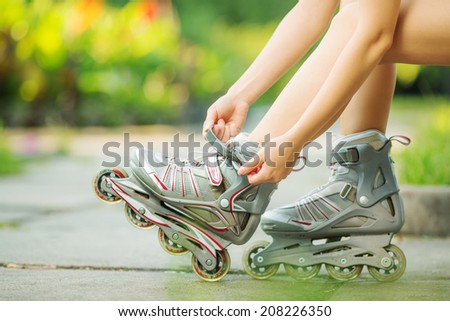 Woman is going rollerblading. Sitting on a bench in a park and putting on inline skates. Close up. Sport lifestyle.