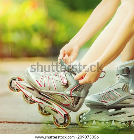 Woman is going rollerblading. Sitting on a bench in a park and putting on inline skates. Close up. Sport lifestyle.