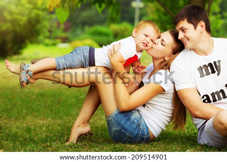 Happy young family is having fun in the green summer park outdoors on a sunny day. Mother, father and their little baby-boy are walking in the park. Love and family concept.