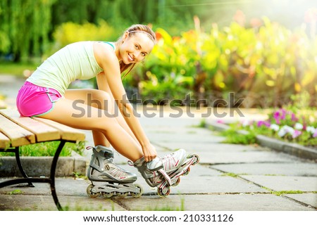 Athletic woman sitting on a bench in a park and putting on inline skates. Close up. Sport lifestyle.