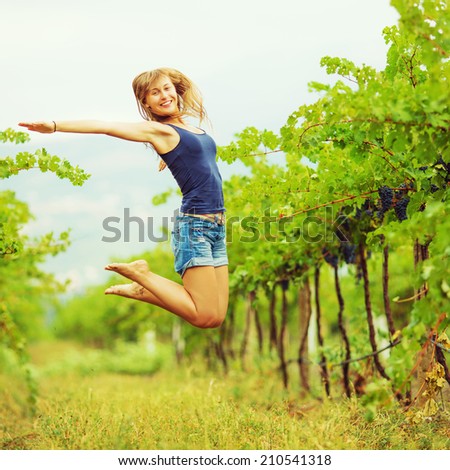 Happy woman in a vineyard is jumping and having fun during the harvest season. Fresh ripe grapes on a vine at the background. Eco lifestyle concept.