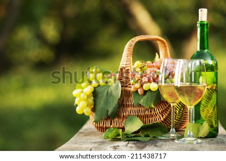 Bottle of wine and grapes on a wooden table. Bottle and full glasses of young white wine are standing on an old wooden table near the basket full of rich organic grapes. New harvest. Space for text