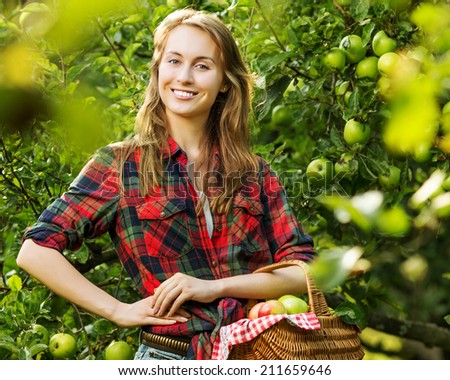 Woman with basket full of ripe apples in a garden. Young smiling attractive woman is standing with full basket of organic apples in a orchard. Country happy lifestyle concept.
