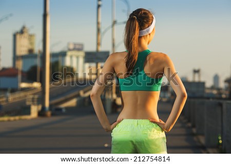 Female fitness model training outside in the city on a quay standing in a sunny bright light on sunrise. Sport lifestyle.