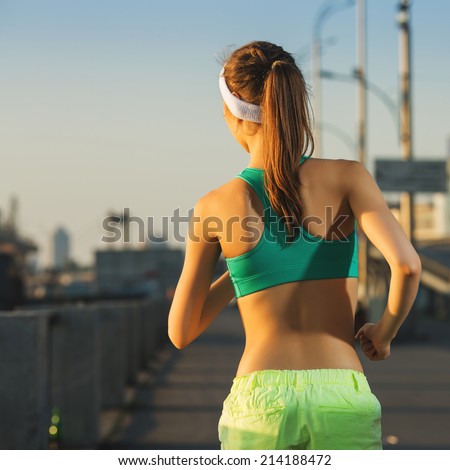 Running woman. Runner is jogging in sunny bright light on sunrise. Female fitness model training outside in the city on a quay. Sport lifestyle. Back view