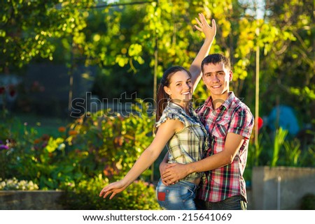 Young couple in love is having fun outdoors. Young beautiful man and woman dressed in casual country style are hugging in a sunny garden. Tender relationship concept.