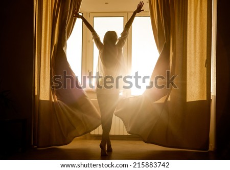 Woman in the morning. Attractive sexy woman with slender body is looking at the sunrise standing near the window in her home and having a perfect cozy morning.