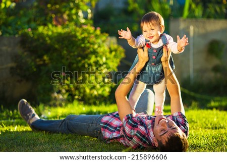 Father and baby daughter are playing outdoors. Young daddy and his cute little baby-girl are having fun in the sunny garden. Happy childhood and parenthood concept. Focus on the daughter.