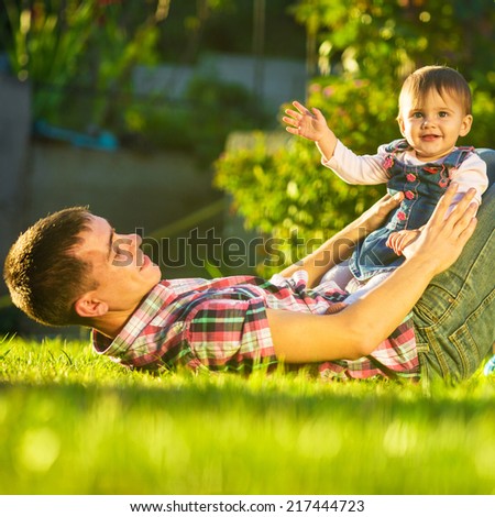 Father and baby daughter are playing outdoors. Young daddy and his cute little baby-girl are having fun in the sunny garden. Happy childhood and parenthood concept. Focus on the daughter.