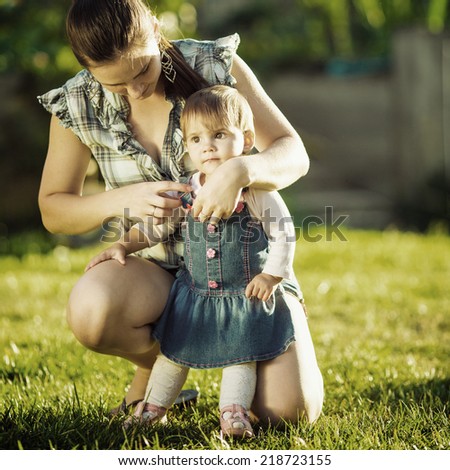 Mother is taking care of her baby daughter outdoors. Young beautiful mother is taking care of her cute baby-girl in the sunlit garden. Family concept. Instagram filter