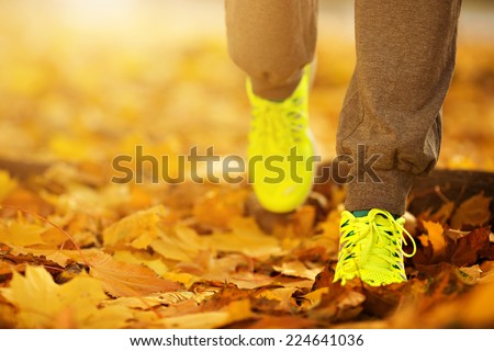 Runner woman feet running on autumn road closeup on shoe. Female fitness model outdoors fall jog workout on a road covered with fallen leaves. Sports healthy lifestyle concept.