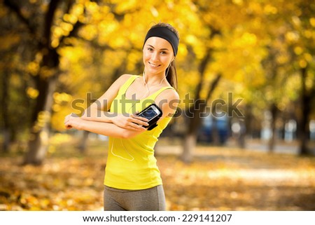 Running woman. Runner is training and listening to music. Female fitness model training outside in the sunny autumn park. Woman athlete resting in the fall outdoors background. Sport lifestyle.