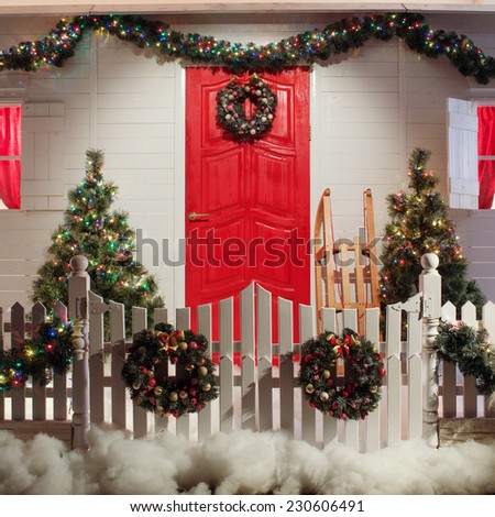 Christmas front door of a country house background. Decorated with lights front door of a pretty house with a white fence. Winter holidays concept.