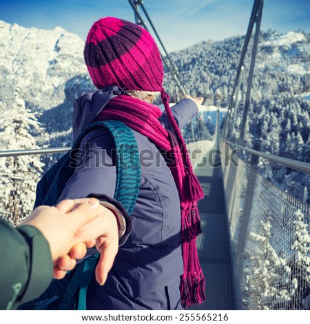 Travel picture from the Austrian Alps in winter. Woman invites her boyfriend to follow her to the longest suspension bridge \