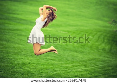 Cheerful woman. Young happy woman jumping with her arms up on a green grass lawn. Attractive woman cheering and enjoying the freedom on a sunny day.