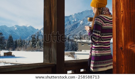 Woman in the morning. Young smiling woman enjoying sunny morning in the Alps mountains drinking tea or coffee on a balcony in the chalet house with a mountain view.