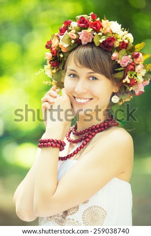 Beautiful woman in a wreath. Young pretty woman wearing a flower wreath in a sunny park outdoors. Spring and summer natural beauty concept.