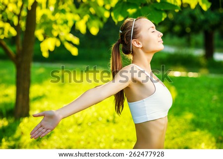 Woman doing sports outdoors.  Young beautiful healthy woman smiling and doing relaxing yoga in the green sunny park. Sports lifestyle and recreation concept.