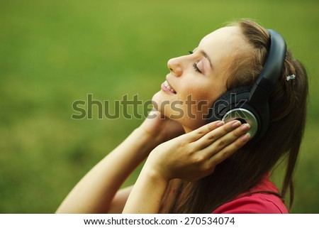 Woman in headphones. Emotional young woman in headphones listening music outdoors on a green grass.