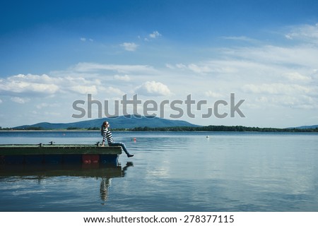 Woman sitting on a wooden jetty enjoying the sunshine.