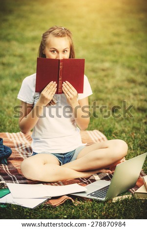 Young woman reading a book outdoors. Beautiful young woman reading a book and studying in the green spring or summer park background. Enjoying a warm day outdoors.