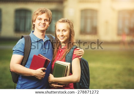 Students standing with books in campus. Young man and woman smiling and standing with books outdoors in sunny spring, summer or autumn.